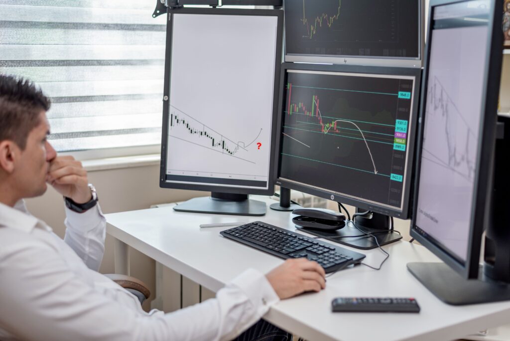Profissional a analisar dados de mercado em múltiplos monitores, representando um agente de monitorização de mercado com IA